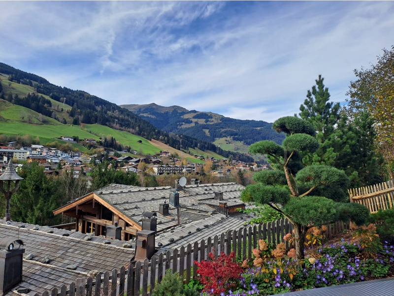 Bunter Garten und Holzzaun hinter traditionellen Tiroler Dächern mit Blick auf die Berge. Gartengestaltung von Schranzhofer in Kitzbühel.